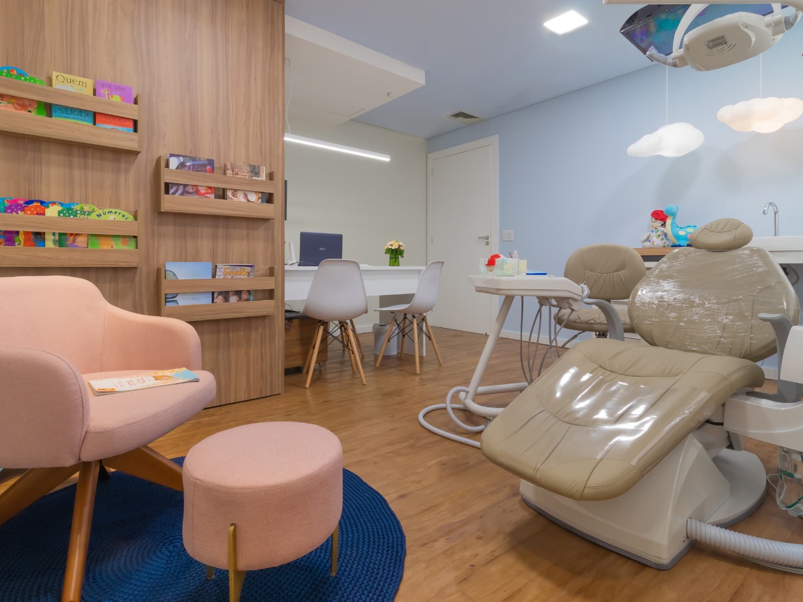 Consultório infantil com livros, poltrona rosa e luminárias de nuvem