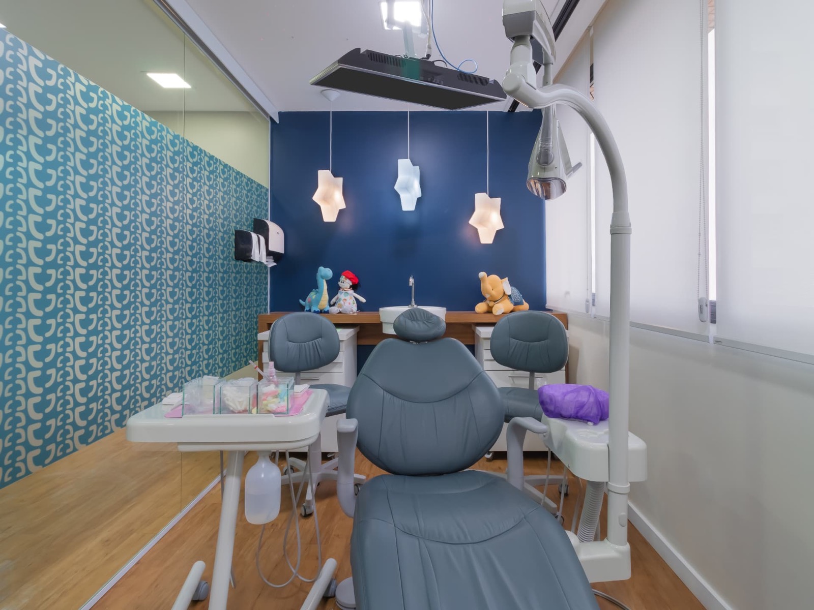 Consultório infantil azul com luminárias em formato de dente e bichos de pelúcia