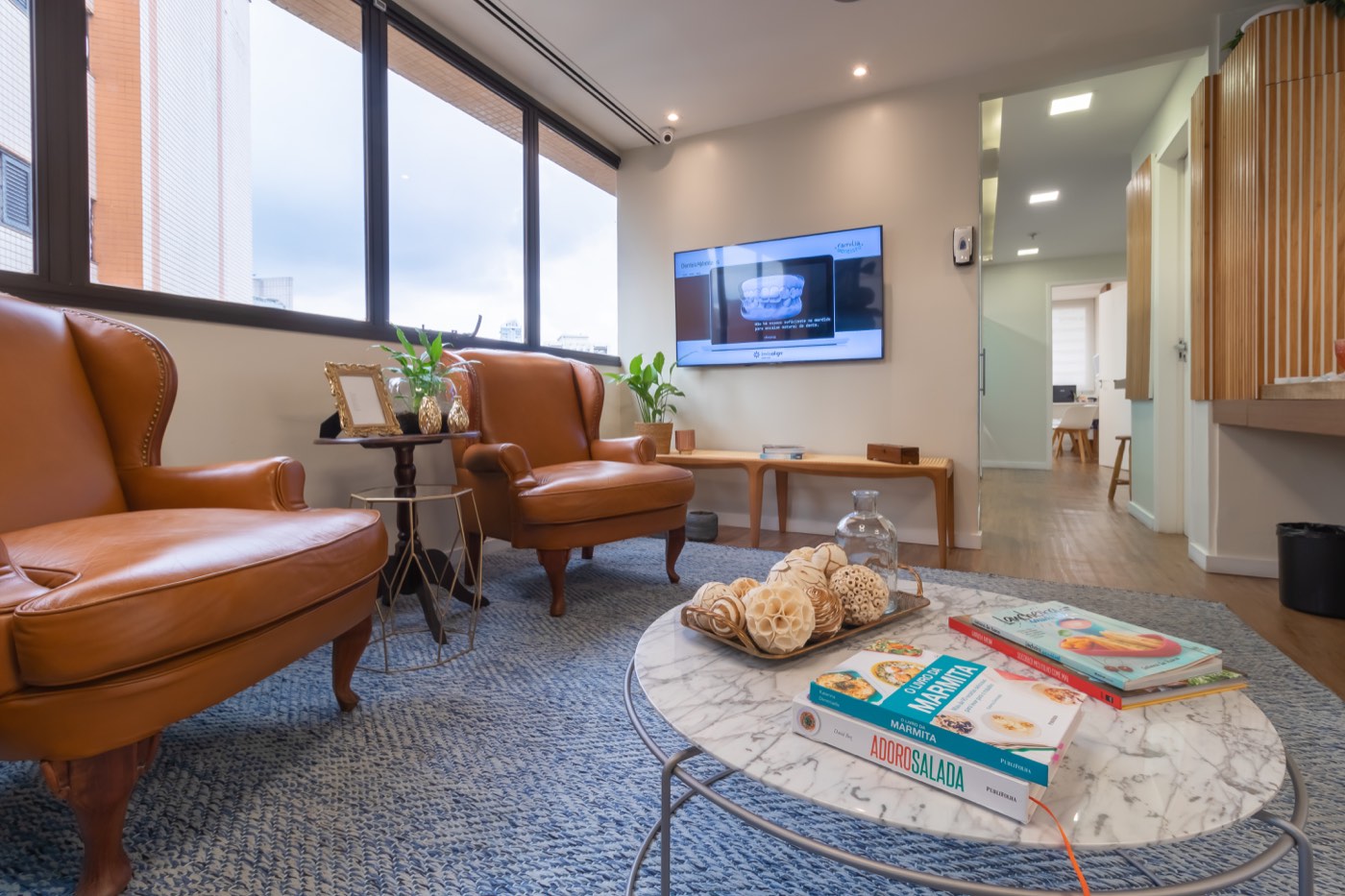 Sala de espera com poltronas de couro caramelo e TV explicando Invisalign